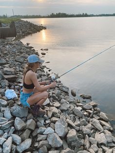 a woman kneeling down on rocks while fishing