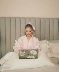 a woman sitting on a bed using a laptop computer while wearing a pink robe and bow in her hair