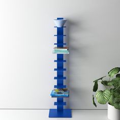 a tall blue shelf with books on it next to a potted plant and white wall