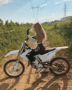 a woman sitting on top of a white dirt bike in the middle of a field