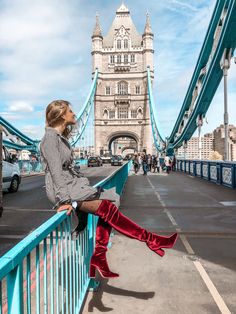 a woman sitting on the edge of a bridge with her legs crossed and wearing red boots