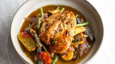 a white bowl filled with chicken, vegetables and gravy on top of a table