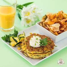 a plate with some food on it next to a glass of orange juice and chips