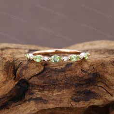 an image of a wedding ring with green stones on it's side, sitting on top of a piece of wood