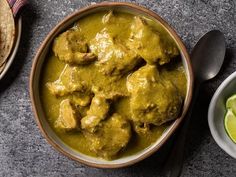 a bowl filled with meat and green sauce next to two bowls of lime wedges