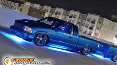 a blue pick up truck parked in a parking lot next to tall buildings at night