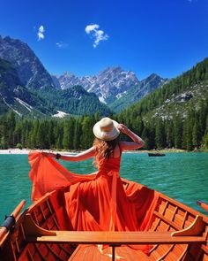 a woman in an orange dress and hat on a boat with mountains in the background