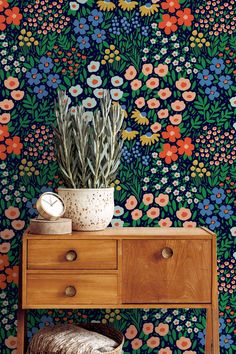 a wooden table topped with a potted plant next to a wall covered in flowers