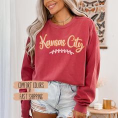 Show off your team spirit with our Women Kansas City Football Sweatshirt Apparel, designed for every KC football fan. This game day unisex pullover crewneck shirt is the perfect Kansas City sport fan clothing for staying comfortable and stylish. ✨𝐏𝐑𝐎𝐃𝐔𝐂𝐓 𝐃𝐄𝐓𝐀𝐈𝐋𝐒✨ ☆ Comfort Colors 1566 unisex sweatshirt ☆ 80% ring-spun cotton, 20% polyester ☆ 1x1 ribbed collar, cuffs, and bottom hem for stretch and a well-fitted garment ☆ Necktape: twill tape stabilizes the neck seam for comfort and Collegiate Team-colored Top With Lettering, Collegiate Tops With Team-colored Lettering, Game Day Sweatshirt With Lettering In Relaxed Fit, Football Season Crew Neck Top With Lettering, Relaxed Fit Lettering Sweatshirt For Game Day, Game Day Fan Apparel Top With Lettering, Football Season Team Spirit Tops With Lettering, Team Spirit Long Sleeve Top With Lettering, Fan Merchandise Lettering Tops For Fall