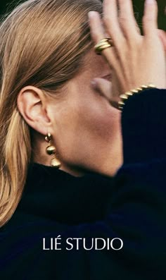 a woman with her hand up to her face and wearing gold rings on her ear