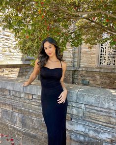 a woman standing next to a tree wearing a black dress