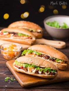 two sandwiches with lettuce, tomato and other toppings sit on a cutting board