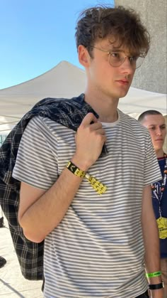 a young man wearing glasses and a striped t - shirt is standing in front of a white tent