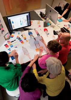 a group of people sitting around a table with paper cutouts on it and computers in the background