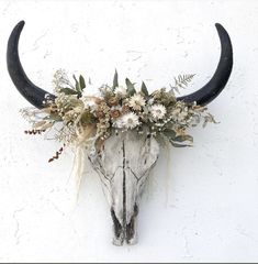 an animal skull with flowers on it's head hanging from the side of a wall