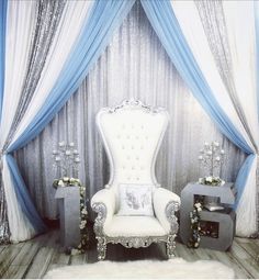 a white chair sitting in front of a blue and white drapeed wall with flowers on it