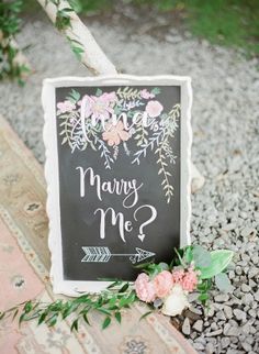 a chalkboard sign that says marry me? with flowers on it and an arrow