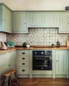 a kitchen with light green cabinets and wood flooring on the counter tops, along with a black oven