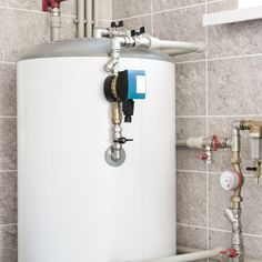 a water heater in the corner of a tiled wall next to pipes and piping