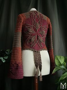 a crocheted sweater on a mannequin with a plant in the background