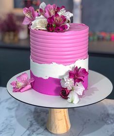 there is a pink and white cake with flowers on the top, sitting on a table