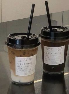 two coffee cups sitting next to each other on top of a metal counter with black straws