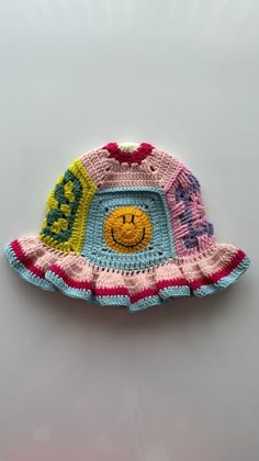 a crocheted hat with a smiley face on the front and bottom, sitting on top of a white surface