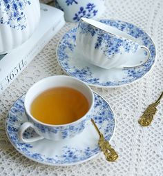 two tea cups and saucers on a white tablecloth with blue floral designs, next to a stack of books