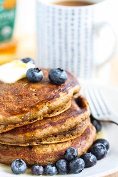 a stack of pancakes with blueberries and butter on a plate next to a cup of coffee