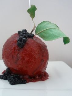 a red apple with blackberries on it sitting on top of a white surface next to a green leaf