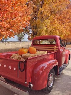 an old red truck with hay and pumpkins in it's flatbed bed