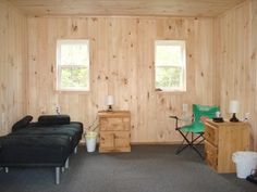 a living room with wood paneling and two black couches in front of windows