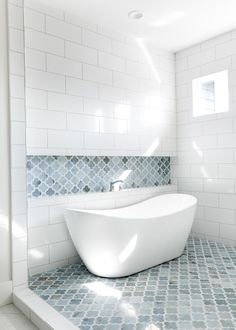 a white bath tub sitting in a bathroom next to a window and tiled flooring