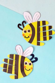 two bees made out of construction paper sitting on top of a blue surface