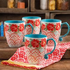 four coffee mugs sitting on top of a wooden table next to a red and white cloth