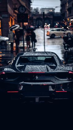 a black sports car parked on the side of a street in the rain with people walking by