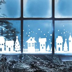 a window that has some paper cut out houses in the windowsill with snow on them