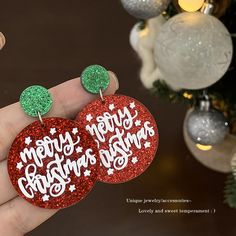 two red and green earrings with merry christmas wishes written on them in front of a christmas tree