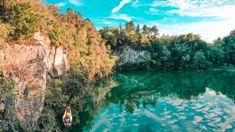 a person on a boat in the middle of a lake surrounded by trees and cliffs