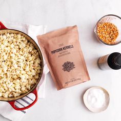 popcorn kernels in a red pot next to other ingredients on a white counter top