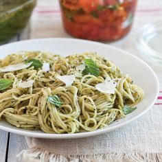 a plate of pasta with basil and parmesan cheese on it next to a jar of tomatoes