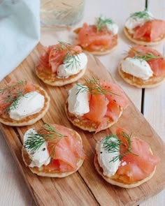 small crackers with smoked salmon and cream cheese on them are sitting on a wooden board