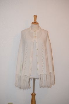 "Dazzle everyone at your next event with this fun beauty. White fine knit cape / poncho by 'Mantessa' features scalloped detail at neckline, front and arm openings as well as double vertical chevron open chevron design down front and back along with extra long fringe. Free of rips, stains and odor. Made in Korea. Measurements: Back of neck to bottom of cape with fringe: 36\" Shoulder to shoulder at back: 20\" Button front: 27 1/2\" Side to side at bottom: 40\" Fringe: 7\" Check out other items i One Size Cream Cape, One Size Cream Poncho, One Size Cream Cape For Fall, One Size Cream Fall Cape, Knitted Cape, Ladies Poncho, Long Fringe, Long Fringes, Chevron Design