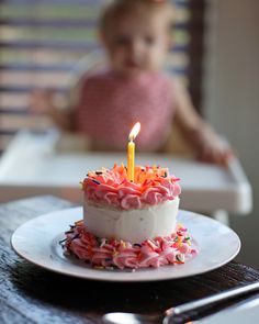 a small child sitting in a highchair behind a birthday cake with a lit candle