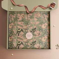 an open box with pink and green designs on the inside, tied in a brown ribbon