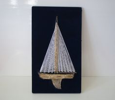 a small sailboat made out of string on a black board with gold trimmings