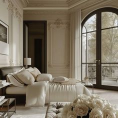 an elegant bedroom with large windows and white flowers on the bed in front of it