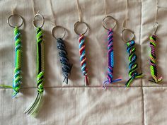 five different colored bracelets hanging from hooks on a white cloth covered tablecloth, all lined up in the same row