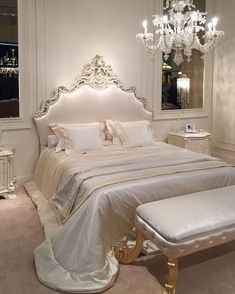 a white bed sitting under a chandelier next to a dresser with drawers on it