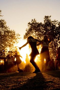 two women dancing in the sun at sunset with trees and people watching them from behind